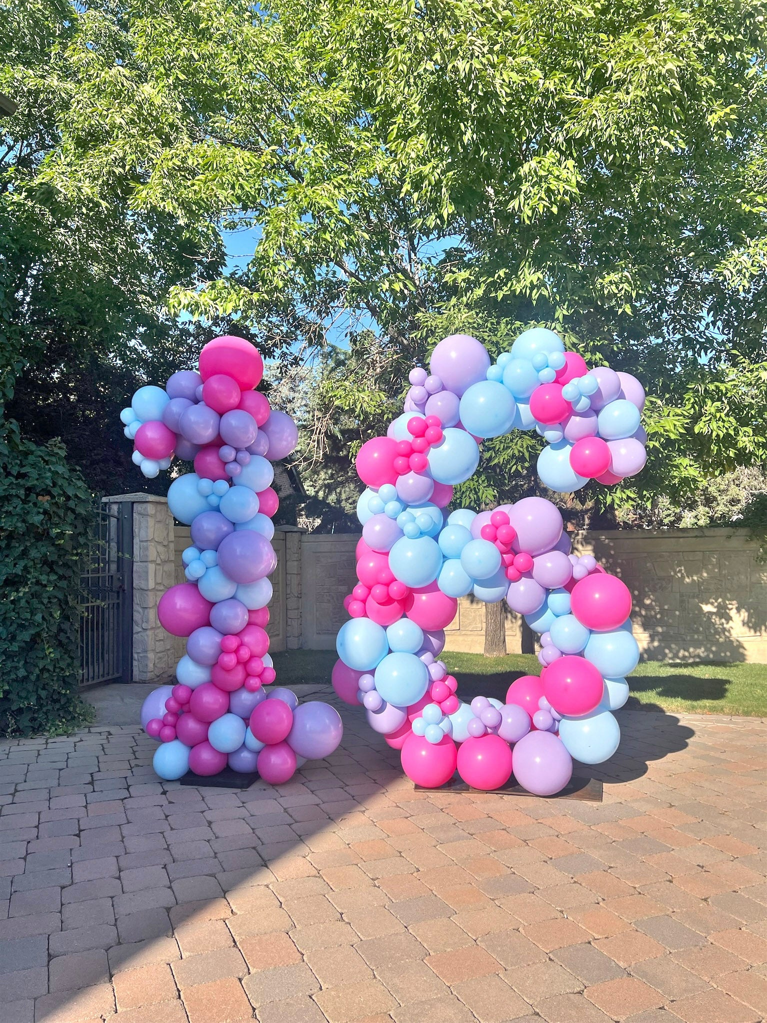 Large yard balloon decor featuring giant number 16 sits in driveway at home in Draper. The giant 16 features Taylor Swift themed colors of fuchsia, pastel blue, pastel purple.