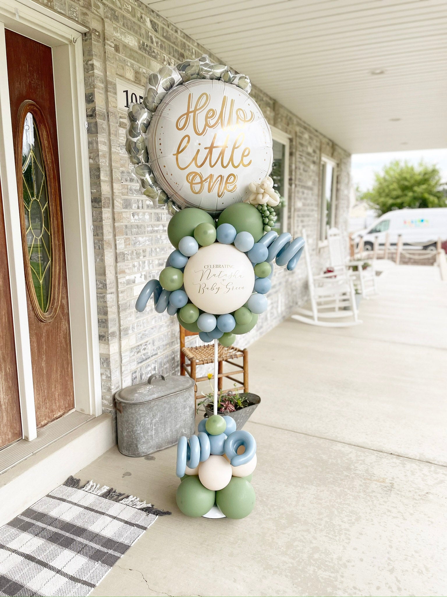Balloon Pole marks entrance to baby shower at baby boy shower in Lehi, Utah. Stand is on the front porch with sage green and light blue balloons around it. "Hello Little One" is on the main big balloon.