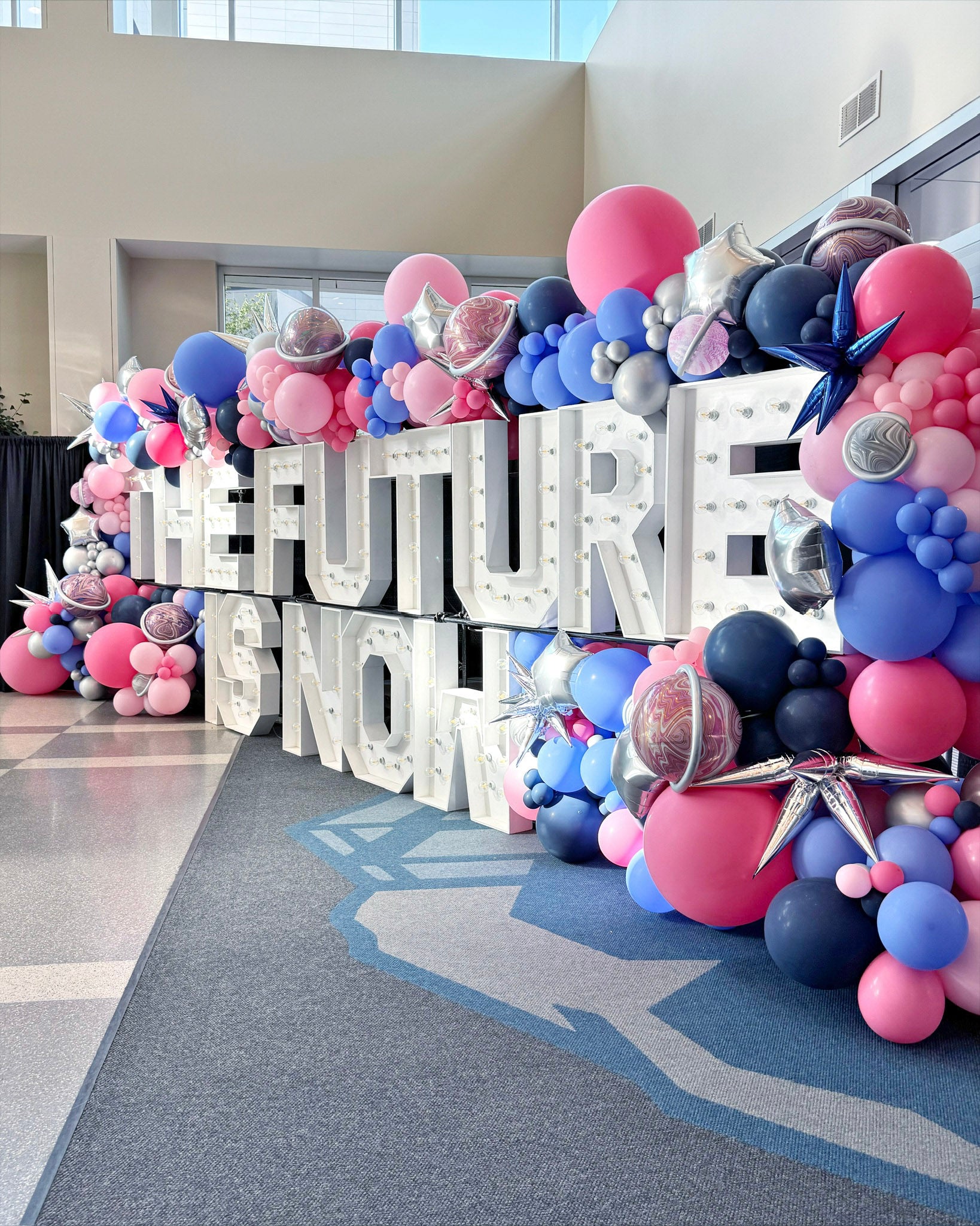 Decorative balloon arch with 'The Future is Now' sign at a Crumbl Owners conference in Provo, Utah