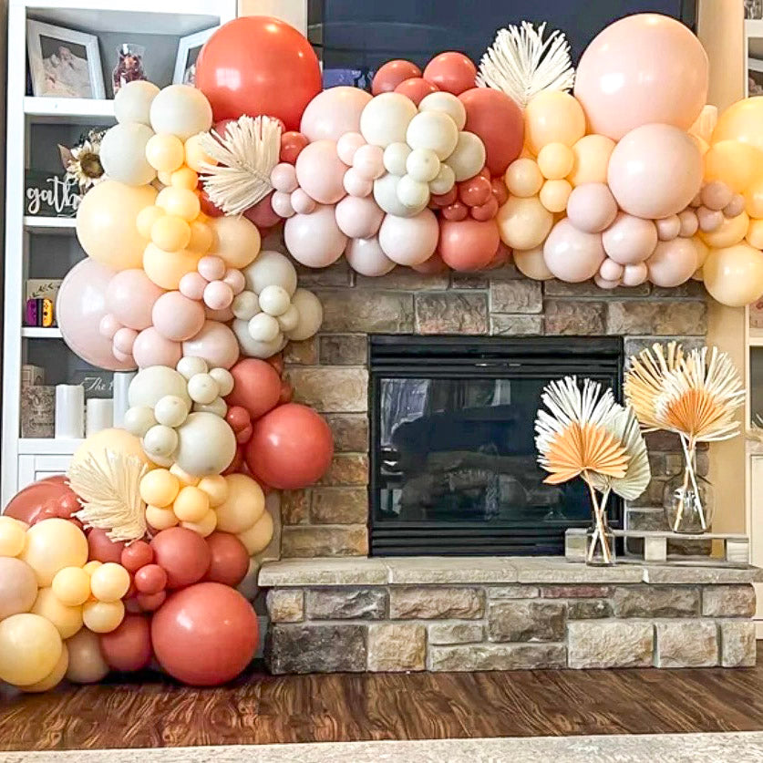 Balloon arch in front of a fireplace with decorative elements featuring the colors burnt orange, blush, peach, and sand