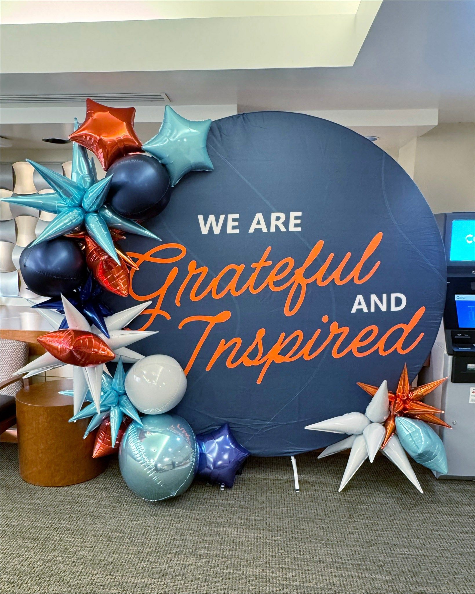 Decorative sign with balloons and text 'WE ARE Grateful AND Inspired' in an indoor setting.