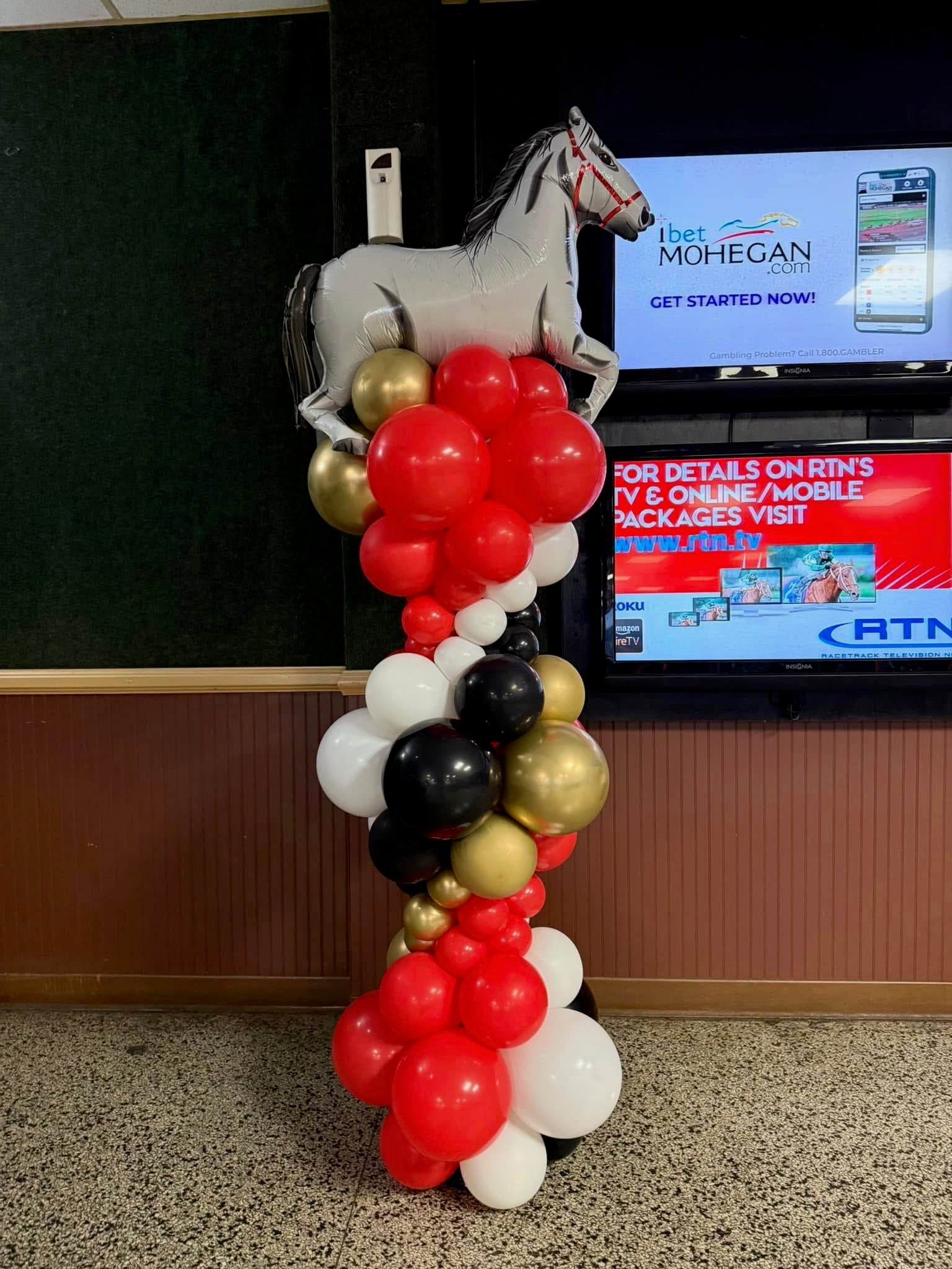 Balloon arch with horse decoration in front of a screen displaying advertisements.