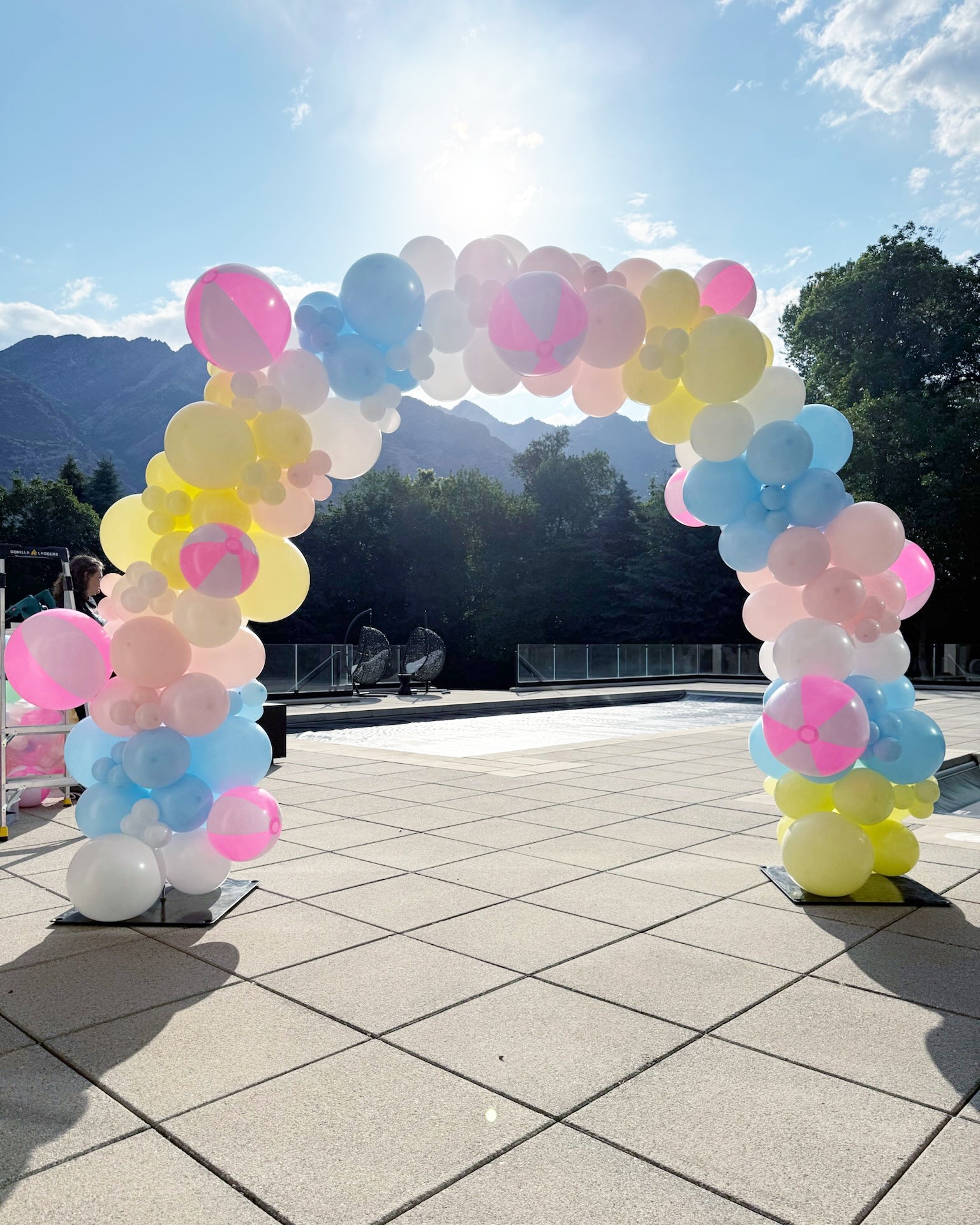 balloons in pastel colors, blue, white, pink, yellow with pink beach balls create an outdoor balloon arch for pool party