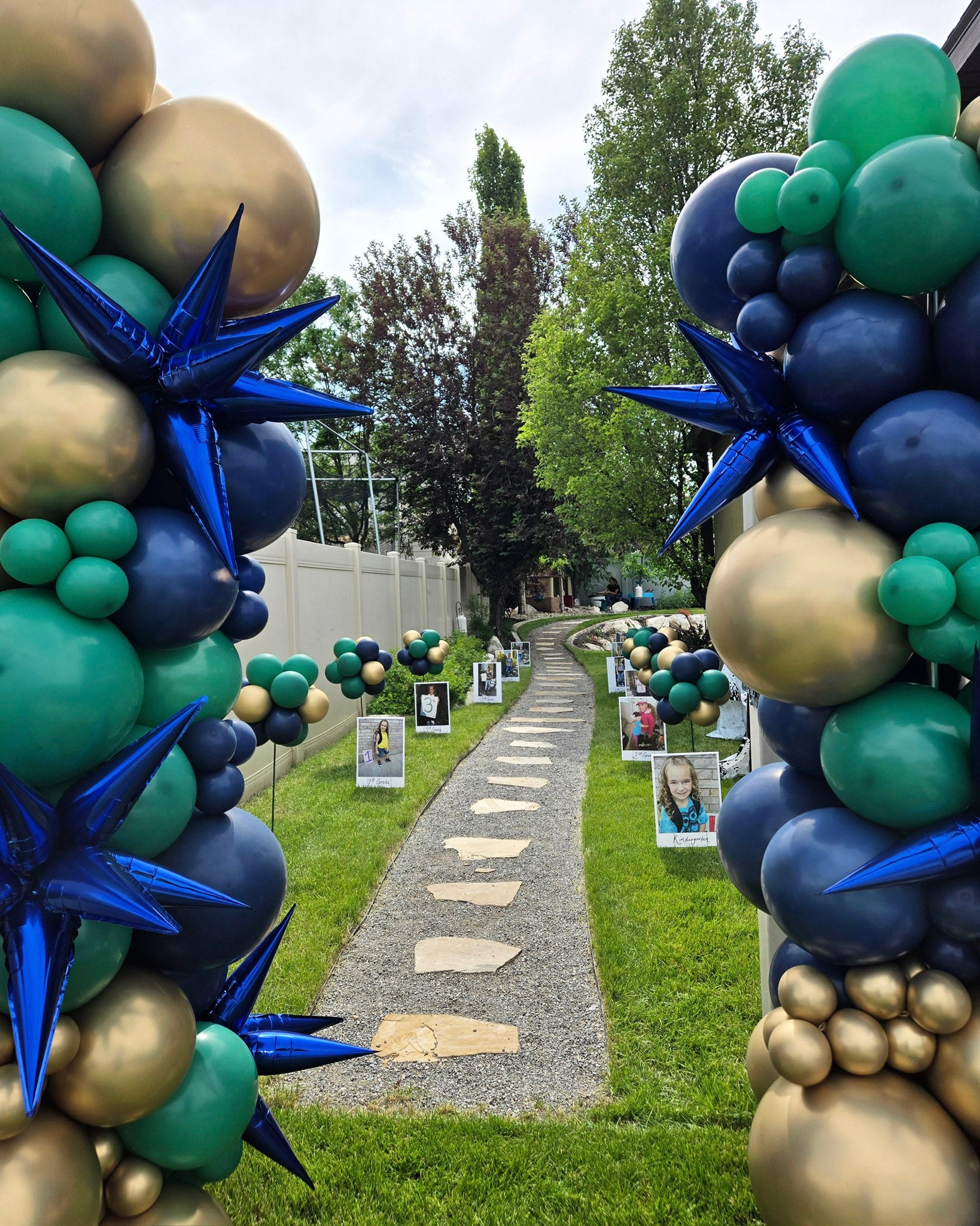 Decorative balloon archway with blue, green, and gold balloons leading to a pathway. Pathway is lined with pictures growing up and balloons and called "Memory Lane"