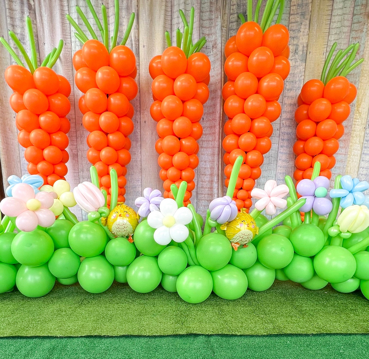 Balloon carrots and flowers arranged in a garden setting with a wooden background.
