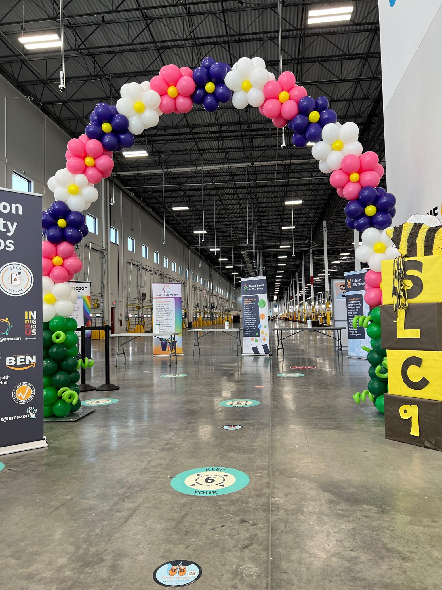 Colorful balloon archway inside a large indoor facility with various signs and banners.