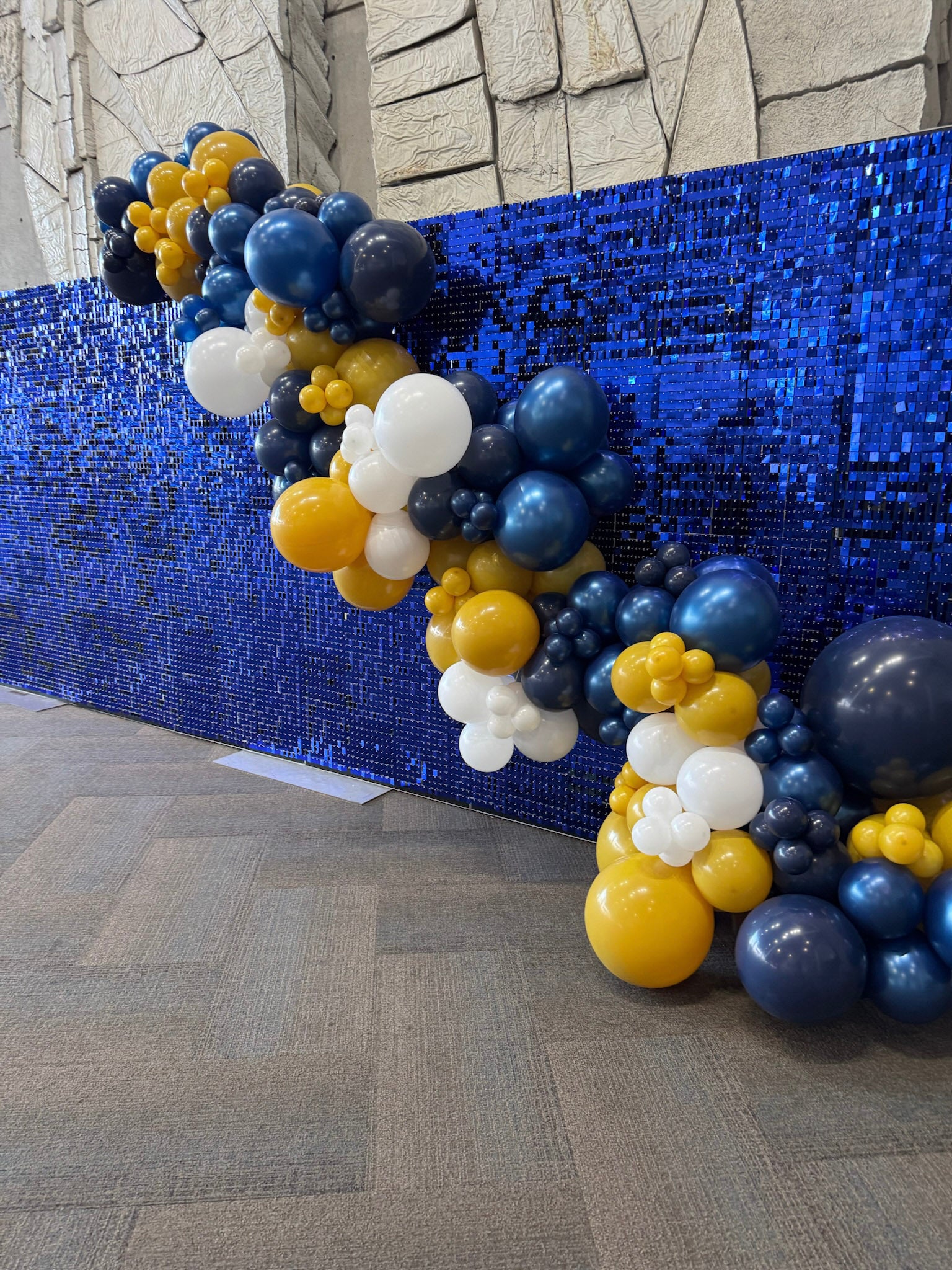 Balloon arch with blue, yellow, and white balloons against a blue sequin backdrop at Mountain America Expo Center
