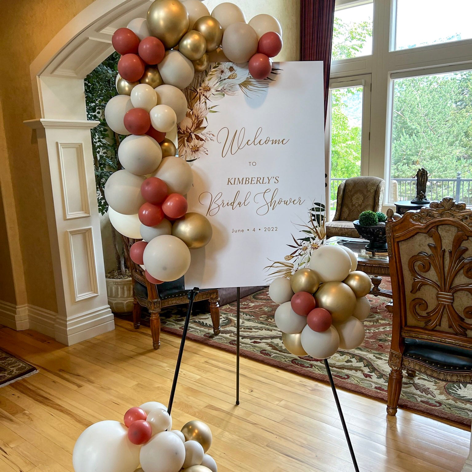 Decorative balloon arch with a welcome sign for a bridal shower in a room with chairs and a table.