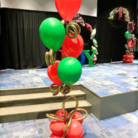 Red and green Christmas helium balloon tower with gold bow accents and a gift-style base, designed by Utah Balloon Creations