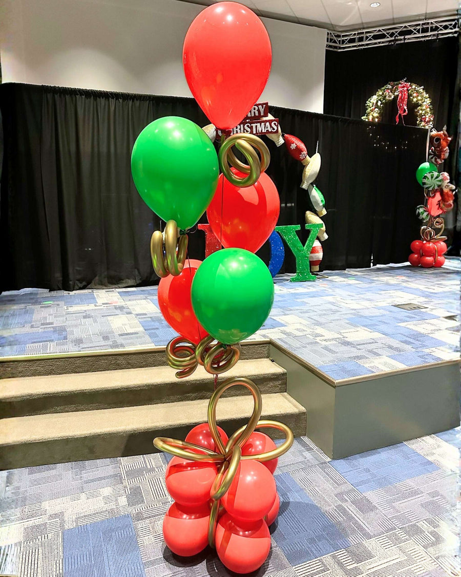 Red and green Christmas helium balloon tower with gold bow accents and a gift-style base, designed by Utah Balloon Creations