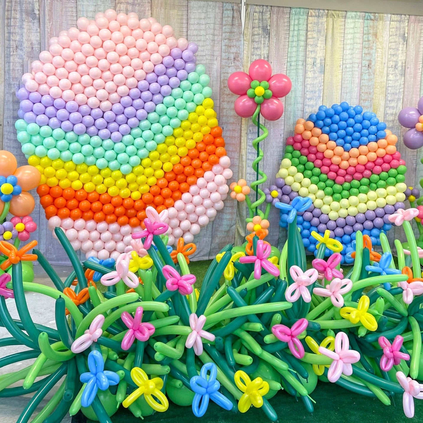 Colorful balloon sculpture of flowers and a rainbow with a wooden backdrop