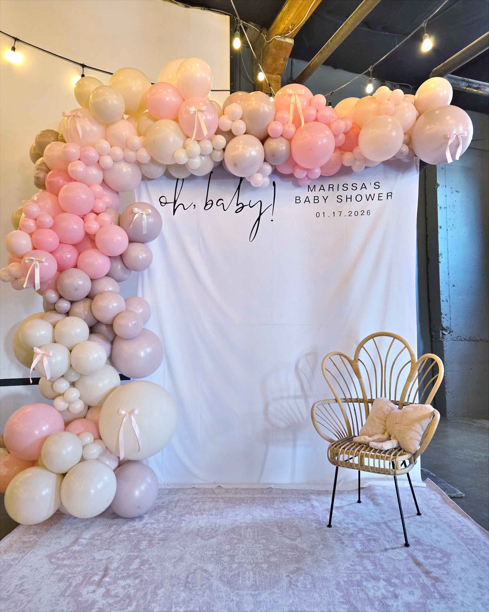 cream, sand, rose, and pink balloon garland goes up and over a backdrop that reads "Oh Baby! Marissa's Baby Shower" at the Startup Building in Provo, Utah
