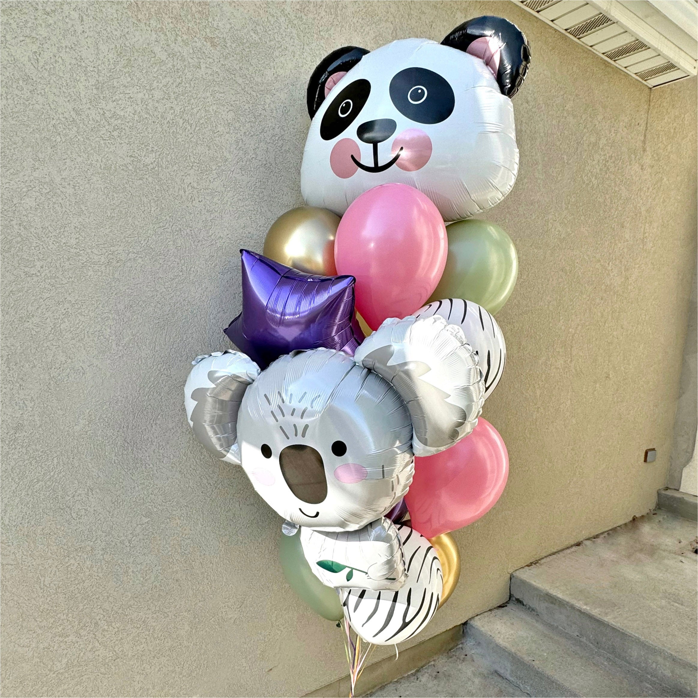 Balloon bouquet with panda and koala balloons against a beige wall.