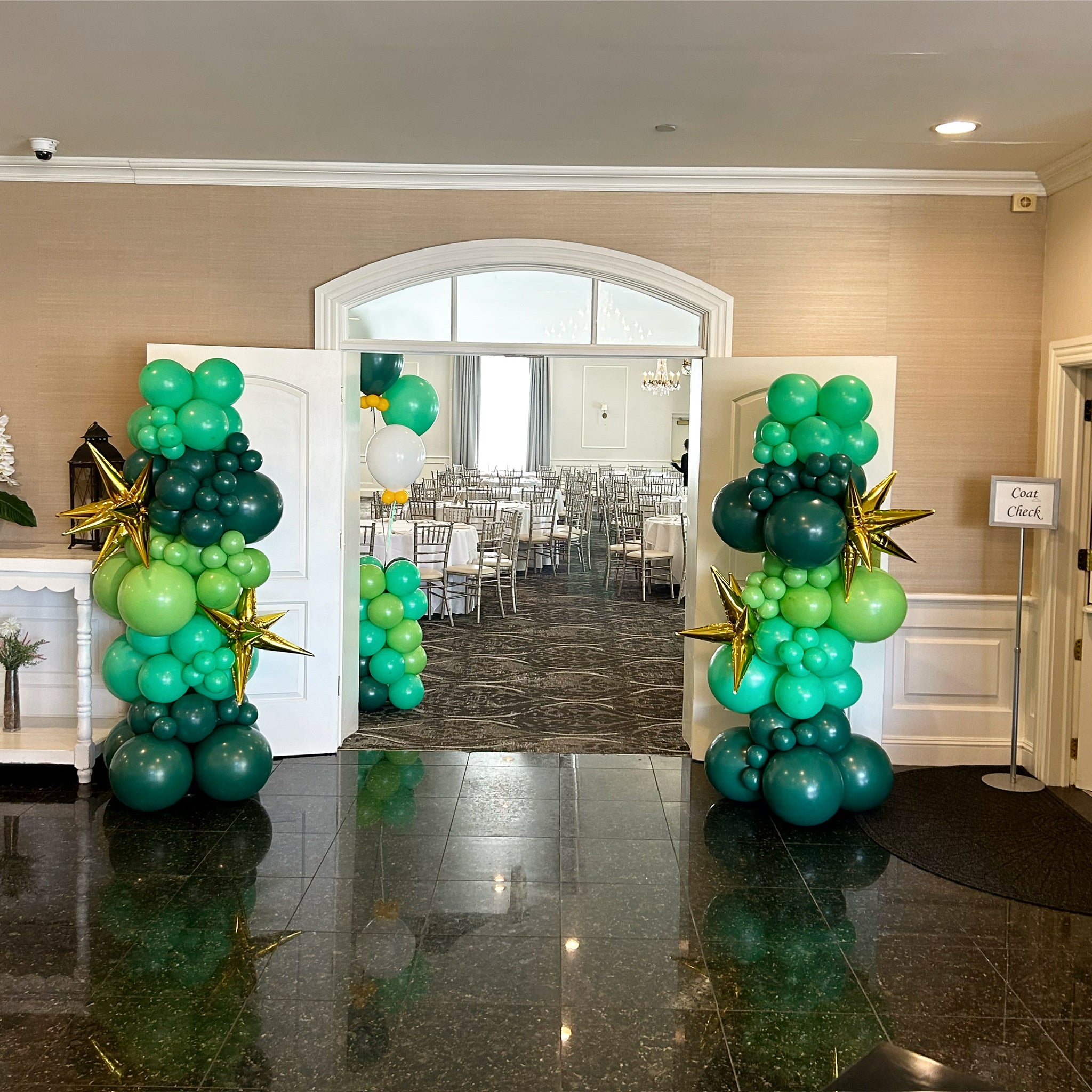 Decorative green balloon columns in a room with chairs and tables.