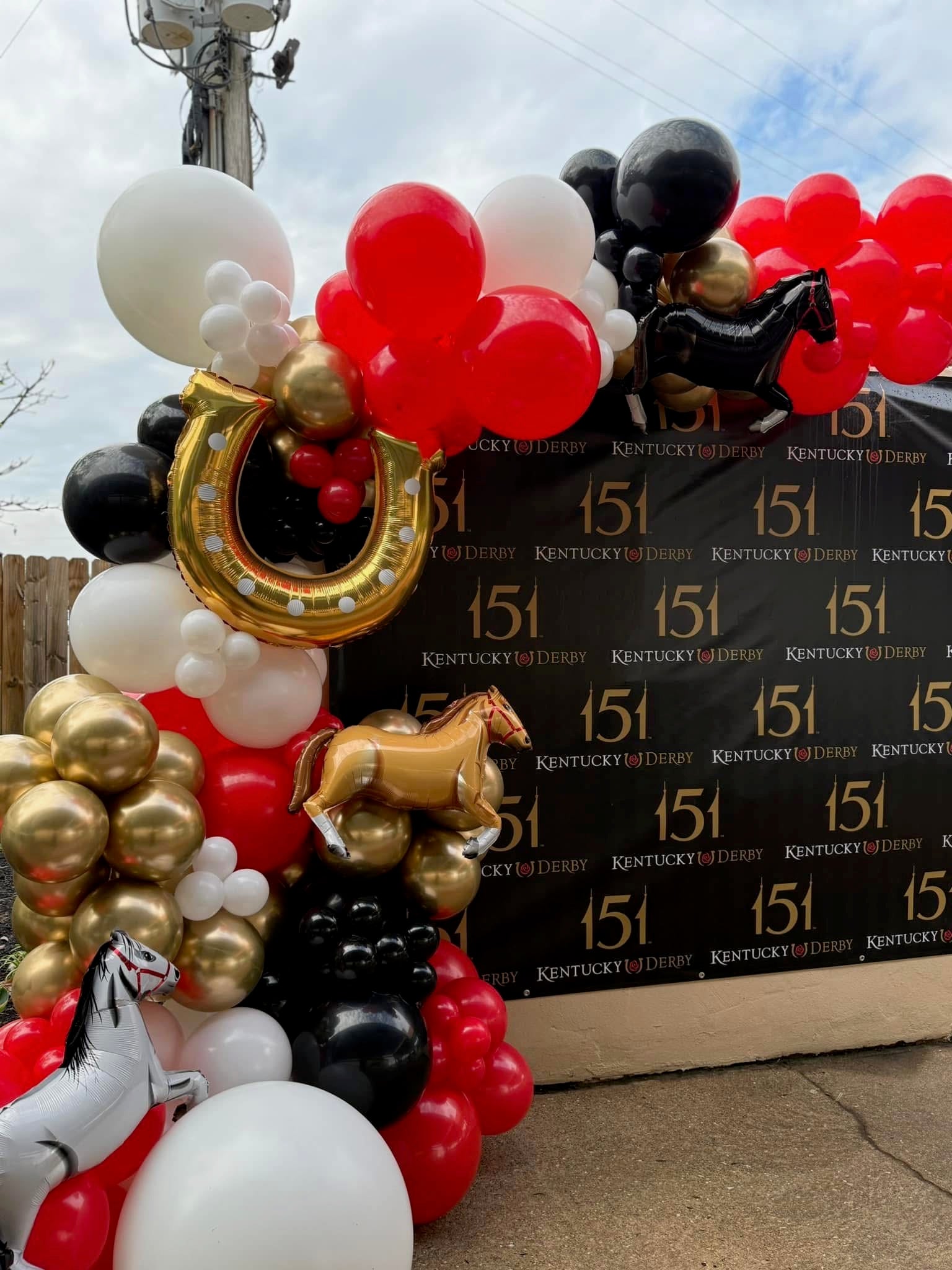 Decorative arch with balloons and horse figures in front of a Kentucky Derby sign.