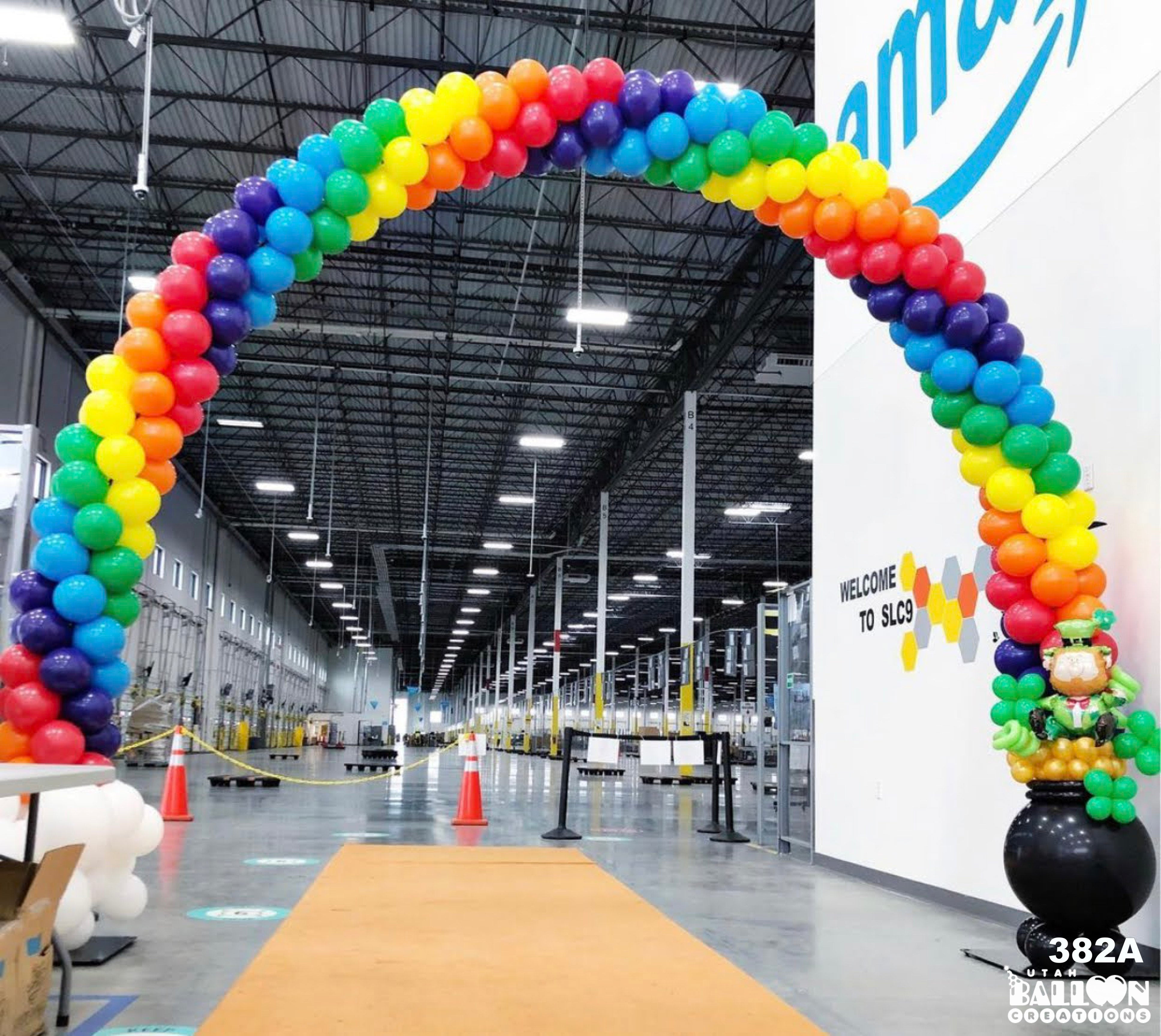 Colorful balloon arch inside a large warehouse with 'Amazon' branding.