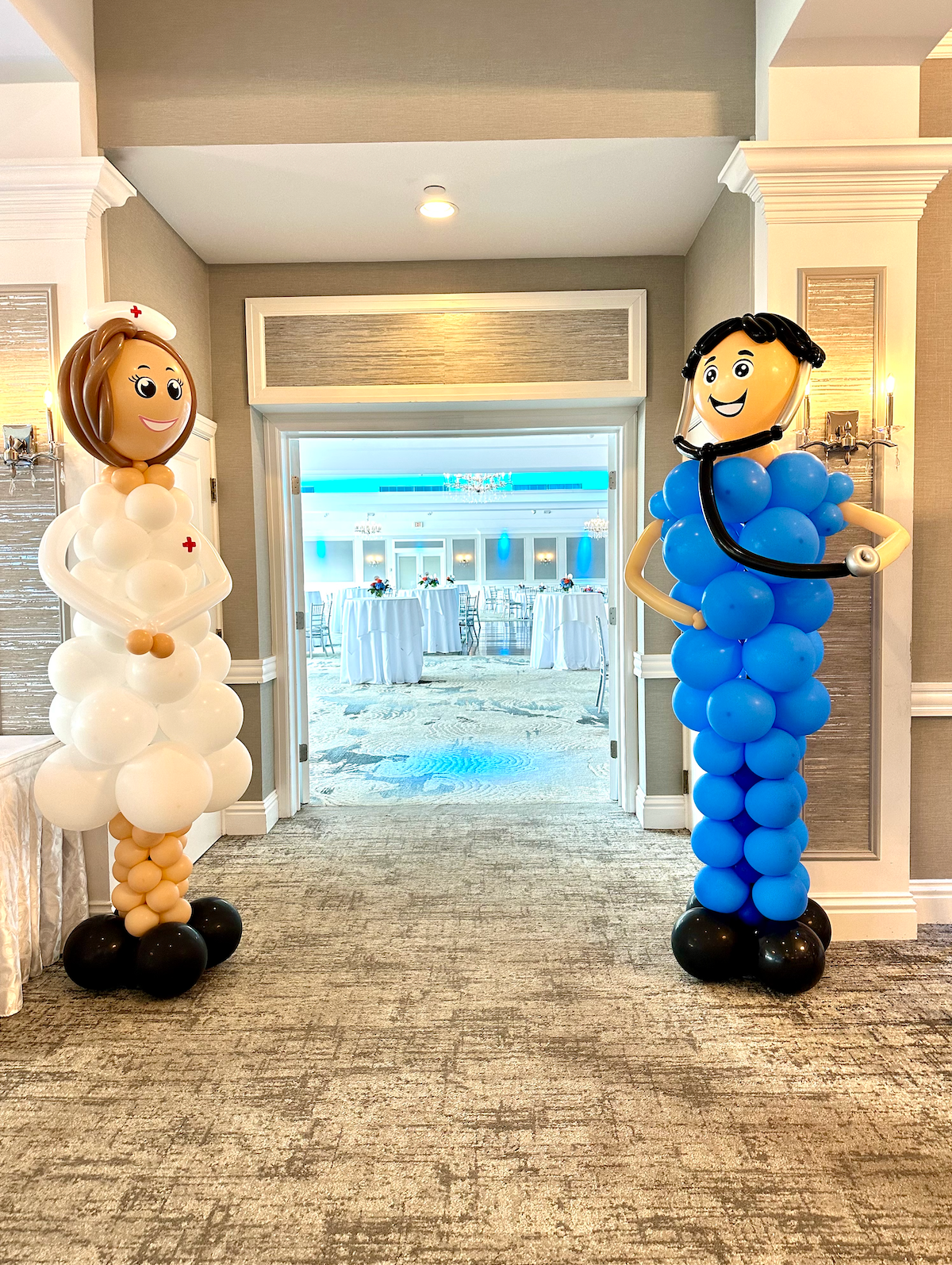 Two balloon sculptures of a nurse and a doctor in a room with a large window.