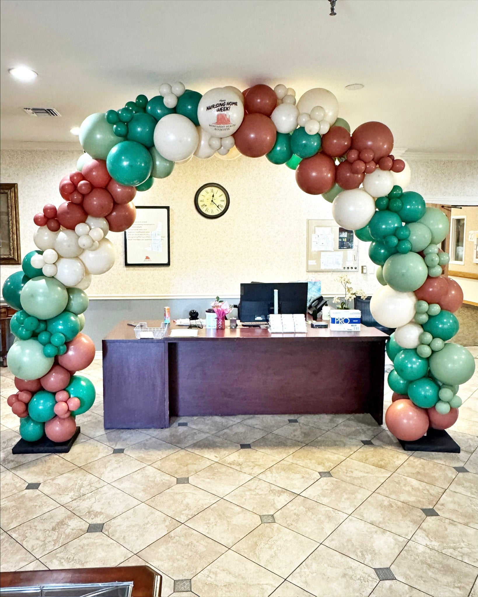 Colorful balloon arch in an office setting with a desk and decor.