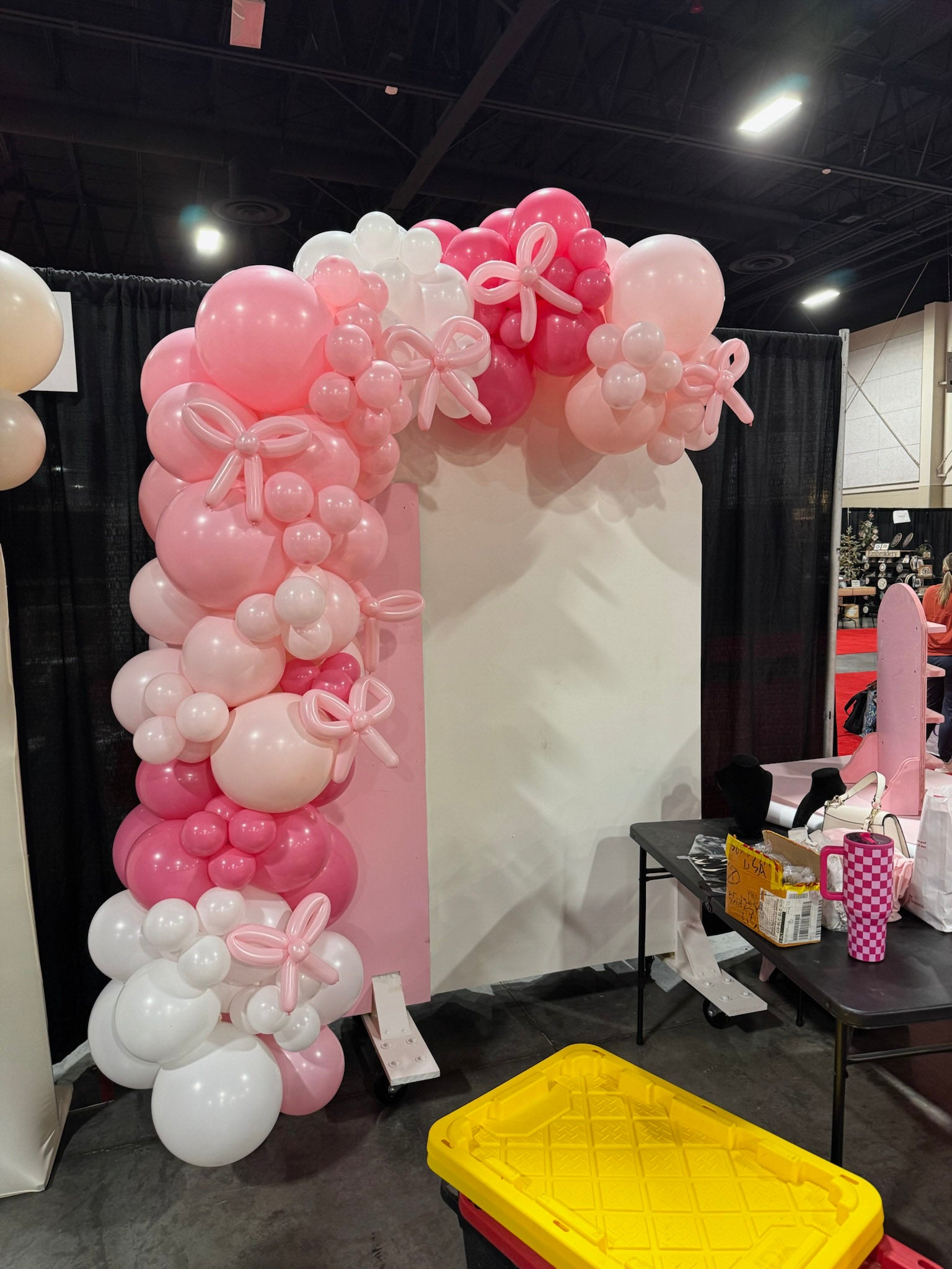 Balloon arch with pink and white balloons and ribbons at an event.
