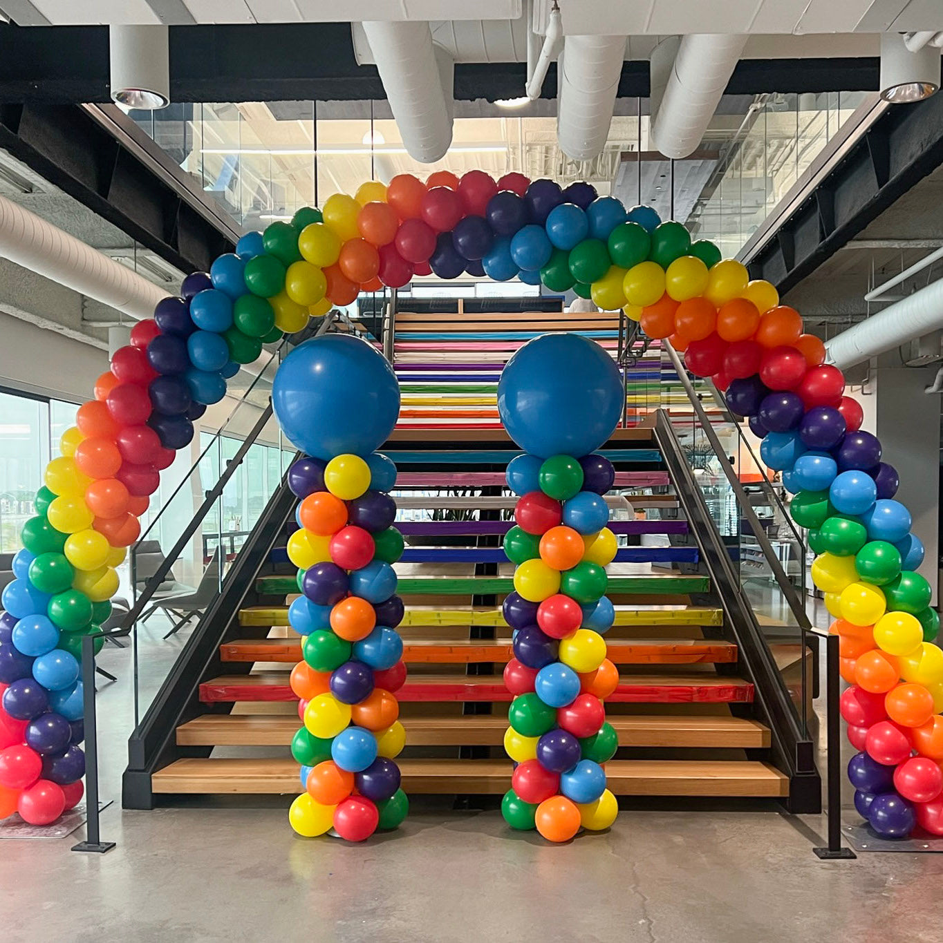 Rainbow balloon arch and balloon columns over staircase celebrating Pride month at corporate location