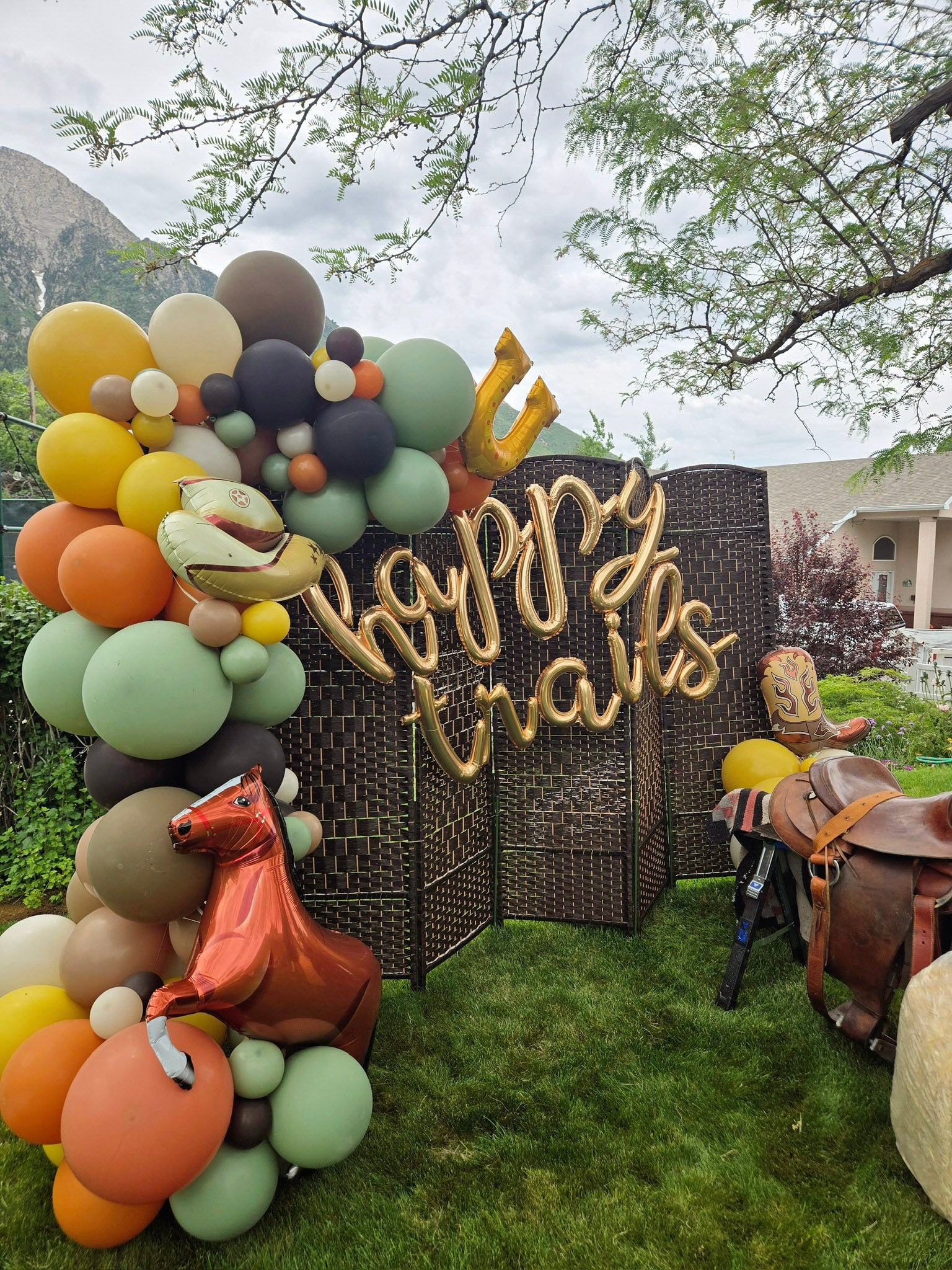 Decorative arch with colorful balloons and 'Happy Trails' sign in an outdoor setting.