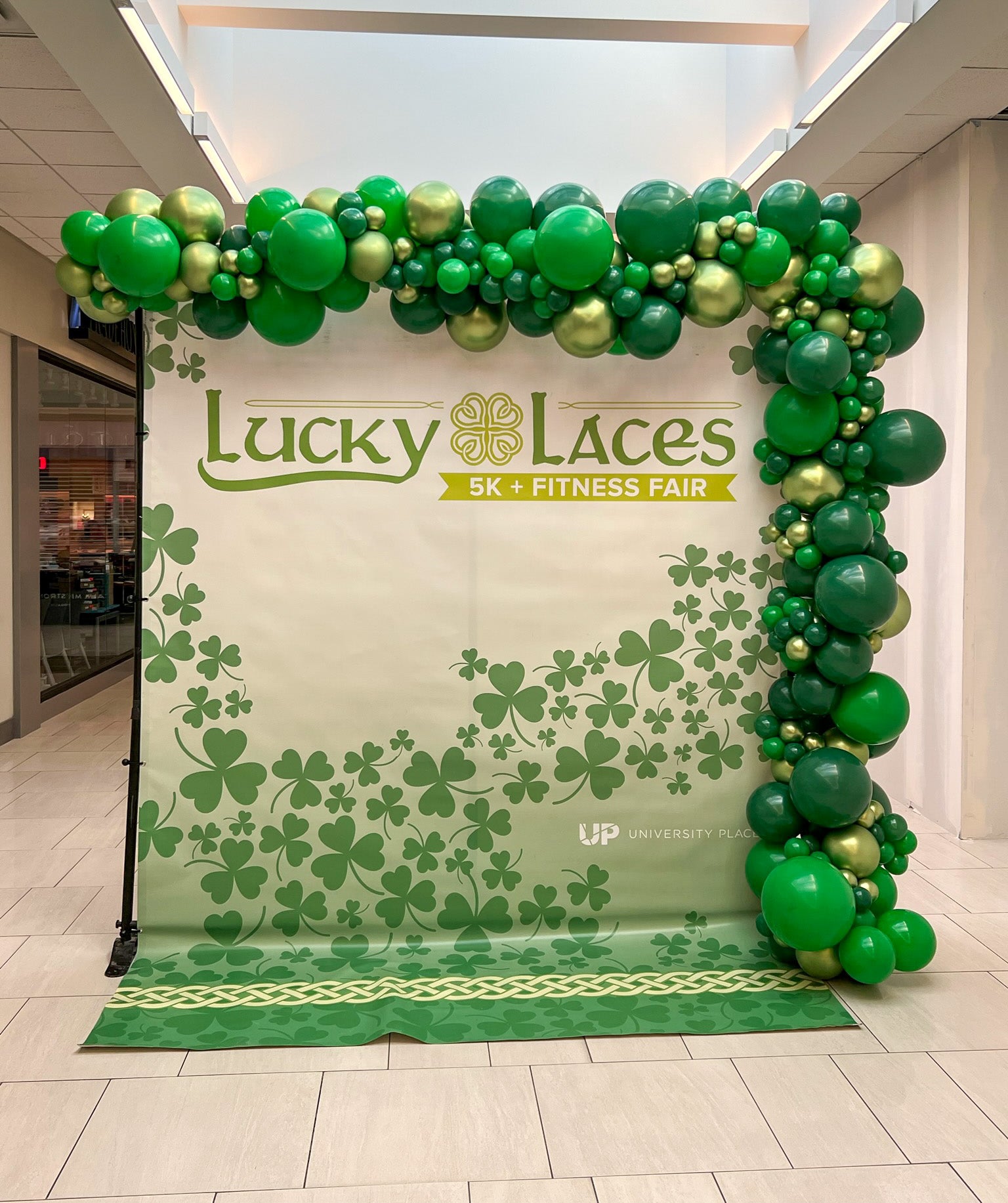 Backdrop with Lucky Laces 5K & Fitness Fair branding and green balloon arch.