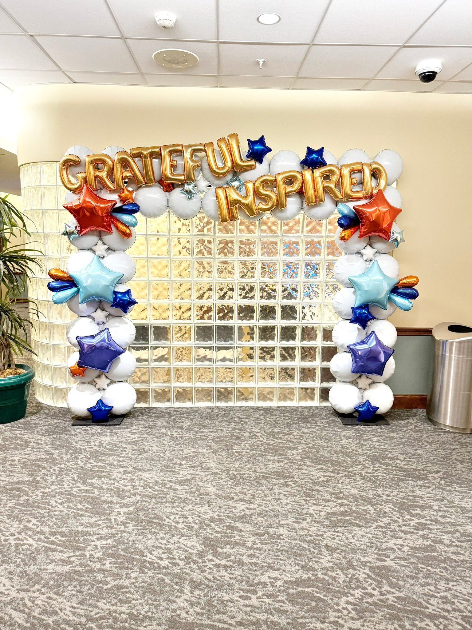 Balloon arch with 'GRATEFUL INSPIRED' text in an indoor setting