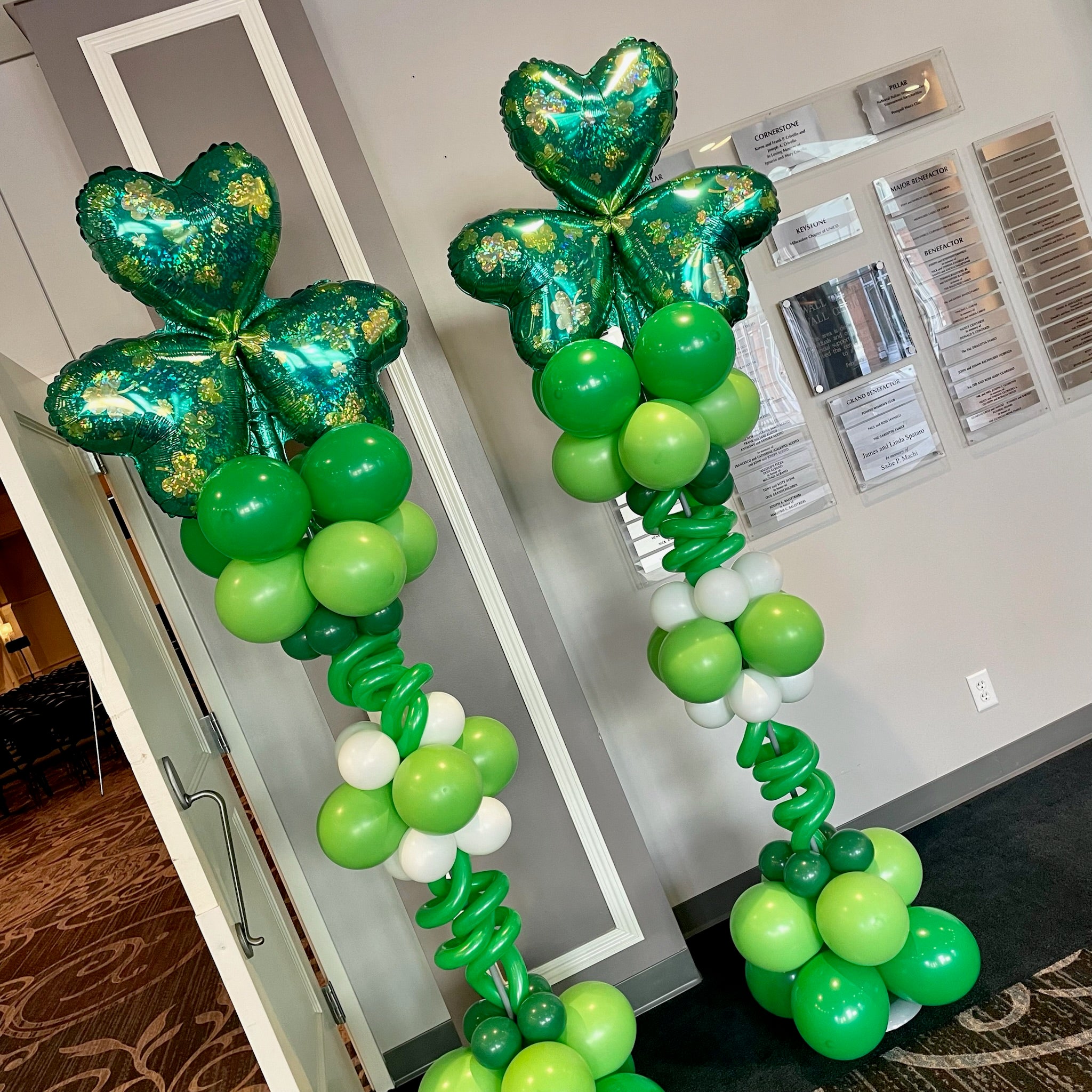Green and white balloon arch with shamrock-shaped balloons in a room setting.