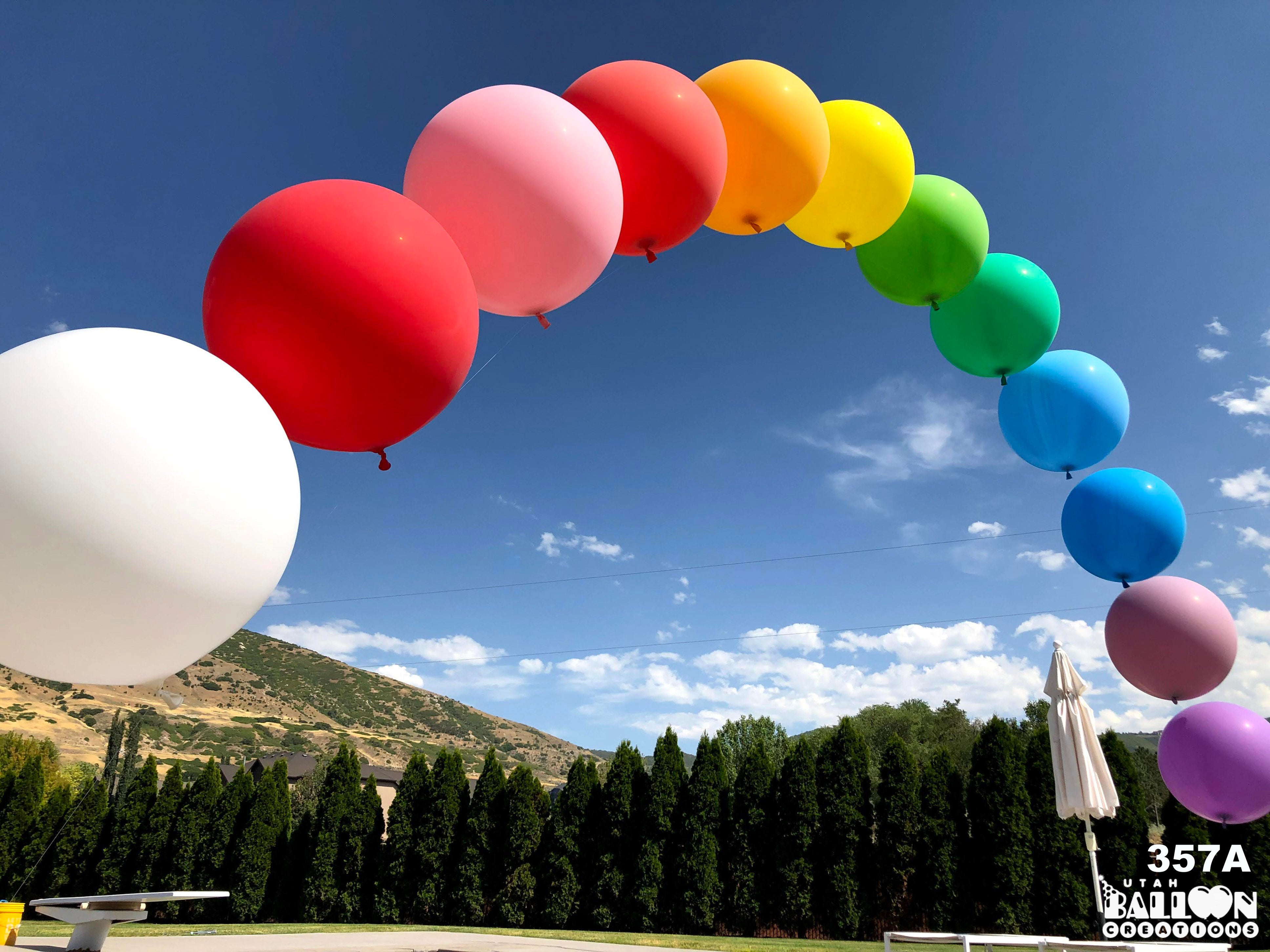 Colorful balloon arch against a blue sky with mountains and trees in the background