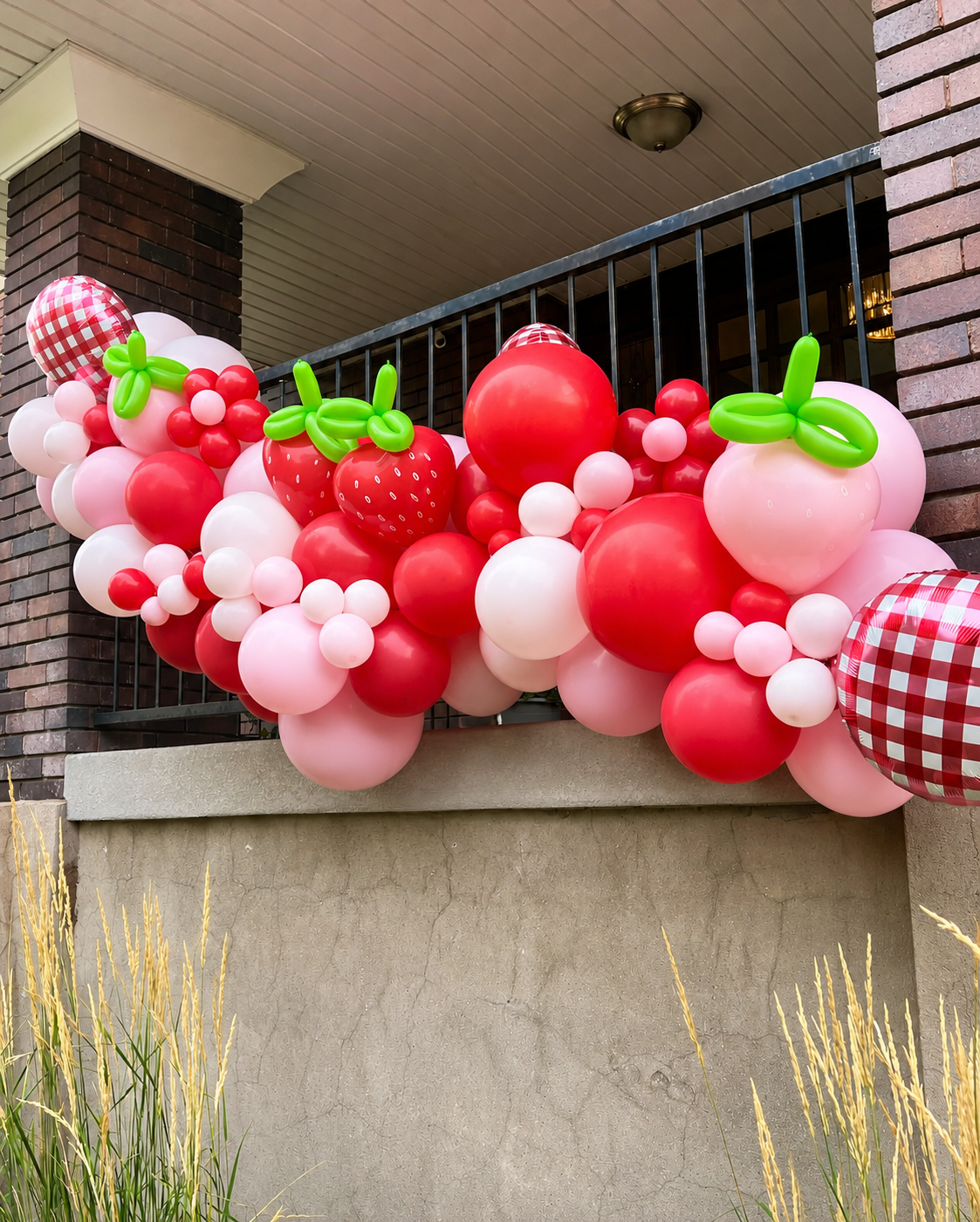 Balloon garland in reds and pinks hang on a front porch for a strawberry summer picnic party