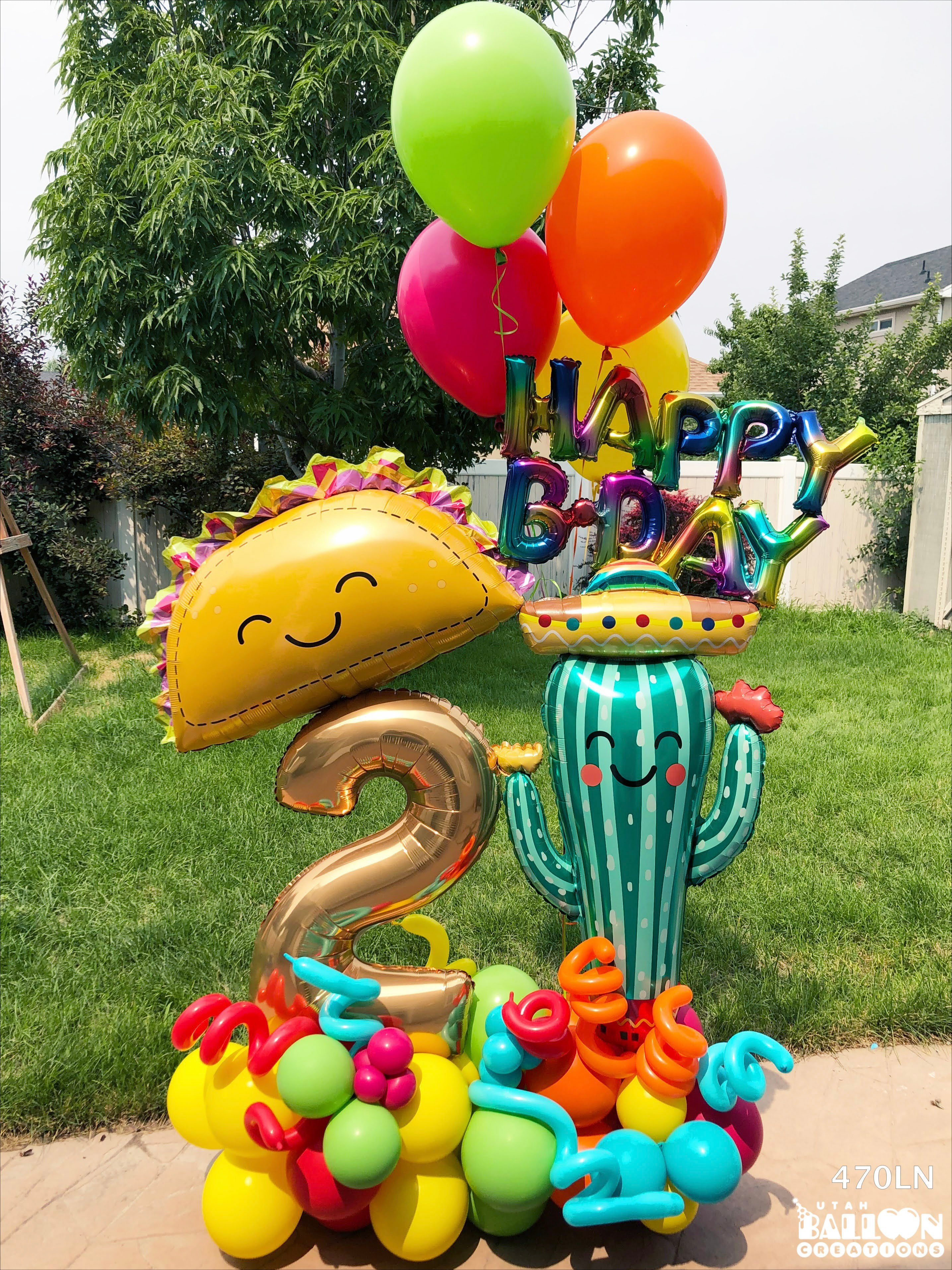 Colorful birthday balloon setup with a cactus, taco, and number 2 balloon on a grassy background.