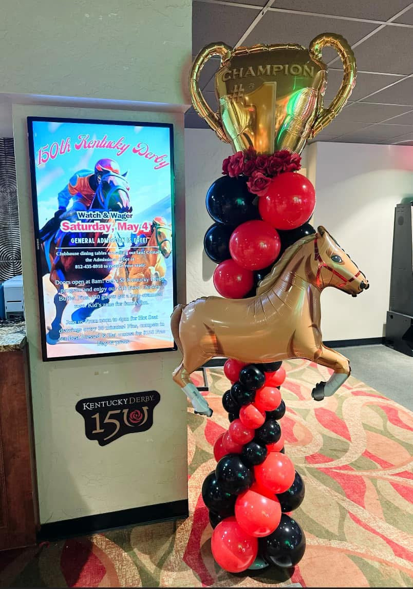 Decorative balloon column with horse and trophy design in front of a screen displaying event information.