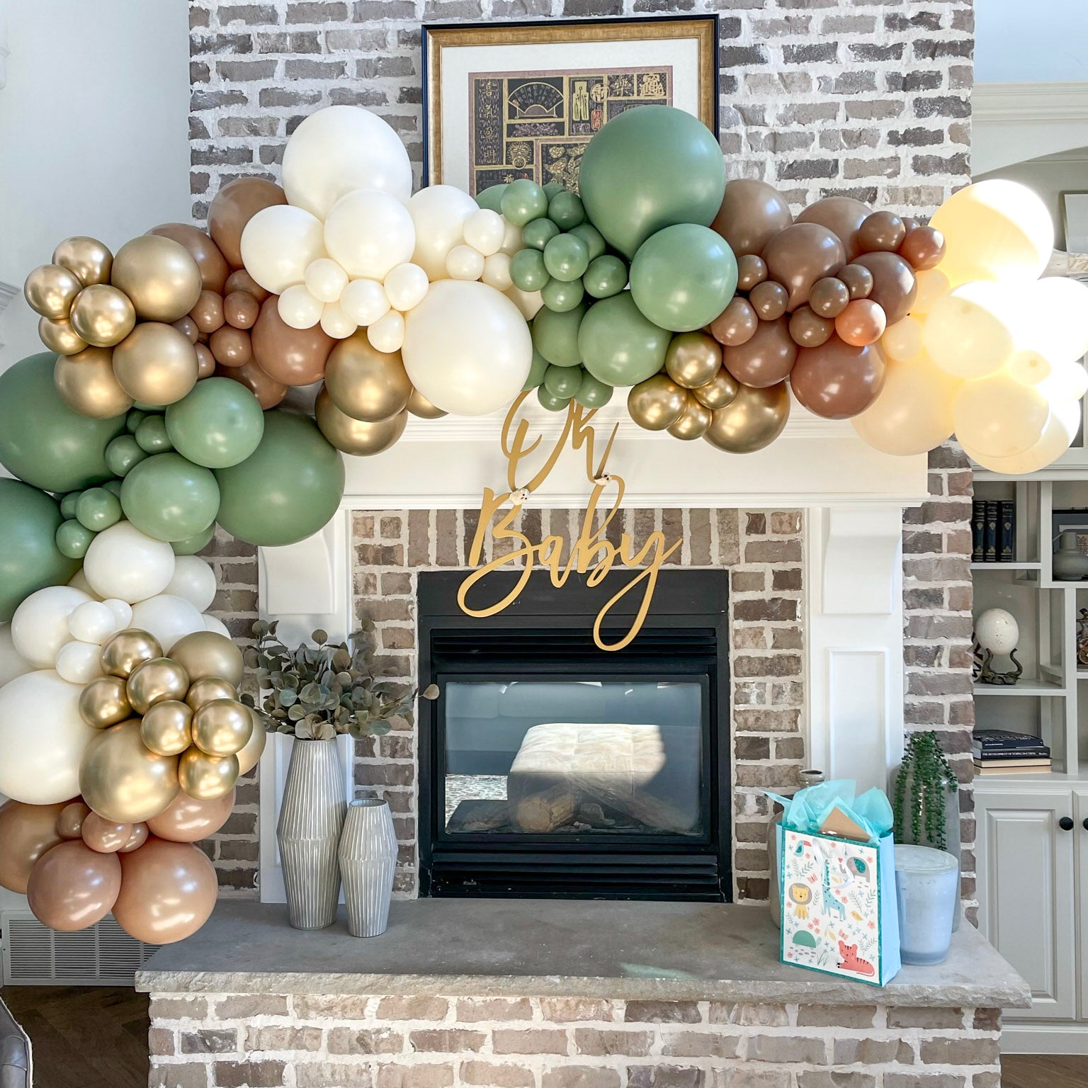 brown, cream, sage green, and gold balloon garland goes up and over a fireplace mantle. An "Oh Baby" sign hangs in the front in Mapleton, Utah.